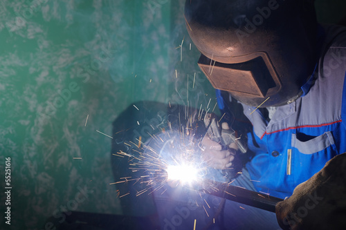 Welder in protective suit and mask welds metal pipes