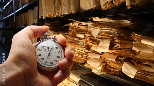 Hand with stopwatch, paper documents stacked in archive