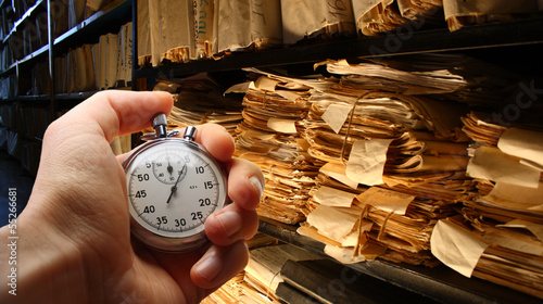 Hand with stopwatch, paper documents stacked in archive photo