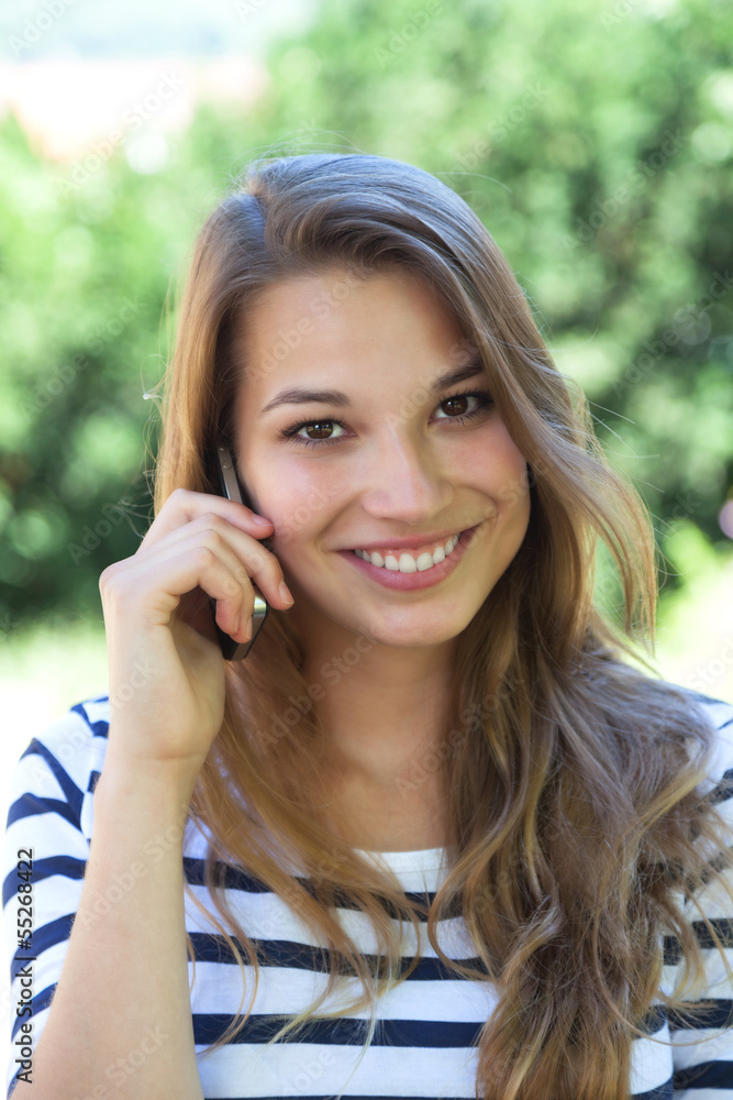 Beautiful young woman smiling on the phone in a park Beautiful young woman smiling on the phone in a park