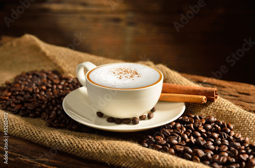 A cup of cappuccino and coffee beans on old wooden background photo