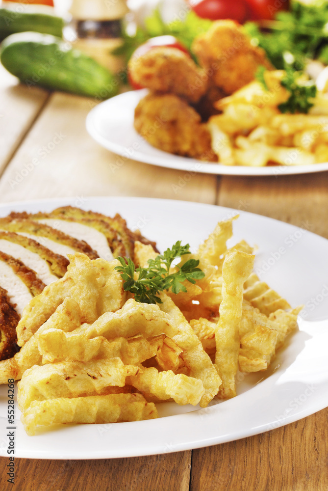 French fries and chicken on the plate on the wooden table French fries and chicken on the plate on the wooden table