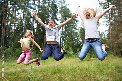 Children jump on lawn in summer forest