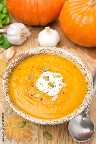 pumpkin soup with coriander and cream on wooden table, top view
