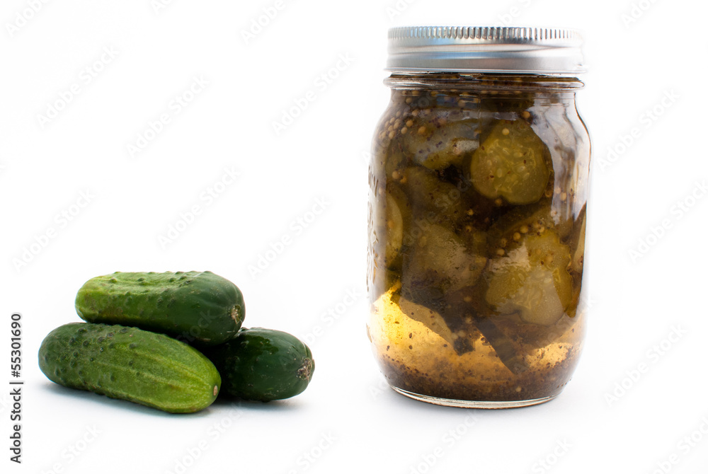 A mason jar of pickles beside fresh cucumbers on a white isolated background A mason jar of pickles beside fresh cucumbers on a white isolated background