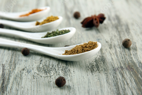 Assortment of spices in white spoons, on wooden background