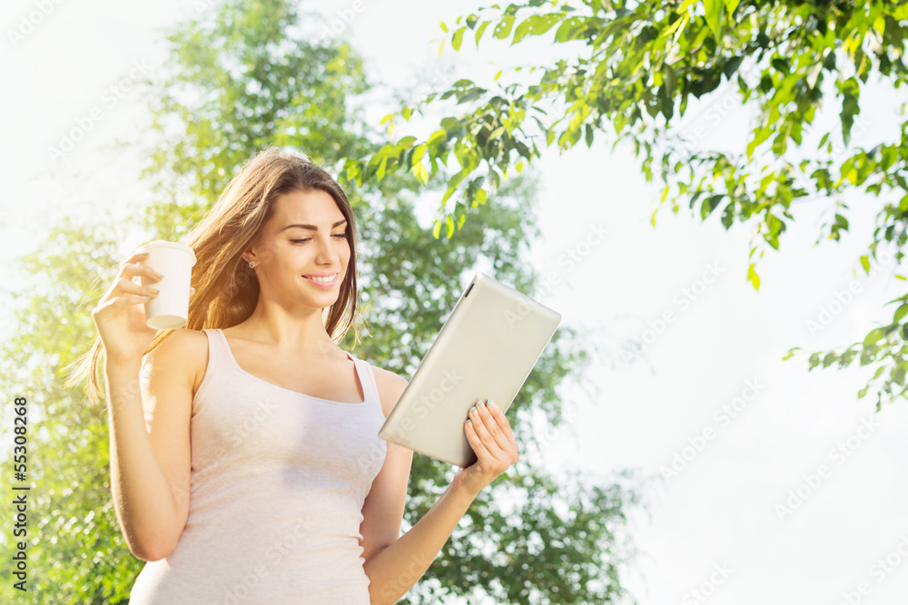 Cute young woman drinking coffee using tablet computer outdoors Cute young woman drinking coffee using tablet computer outdoors