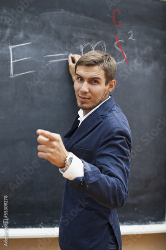 young teacher writing on a blackboard with chalk