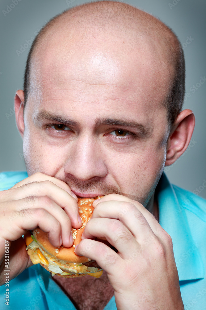 Funny man eating hamburger on grey background Funny man eating hamburger on grey background