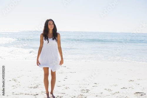 Happy brunette in white sun dress walking on the sand