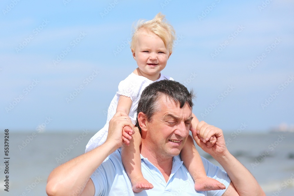 Cute baby sitting on papa's shoulders on the beach at sea Cute baby sitting on papa's shoulders on the beach at sea
