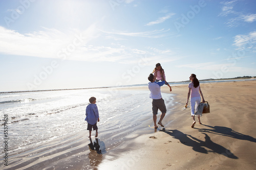 Rear View Of Family Walking Along Beach With Picnic Basket