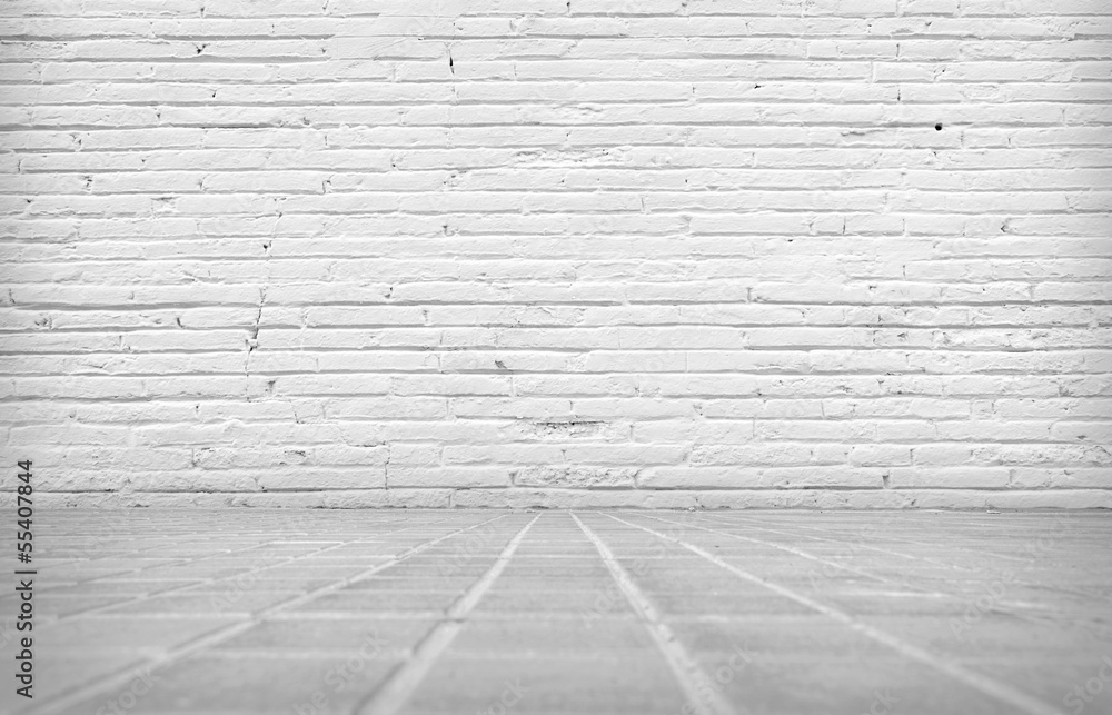 Fototapeta premium A textured white brick wall and a grey concrete floor are viewed from a low angle, creating an old grunge background with a rustic feel.