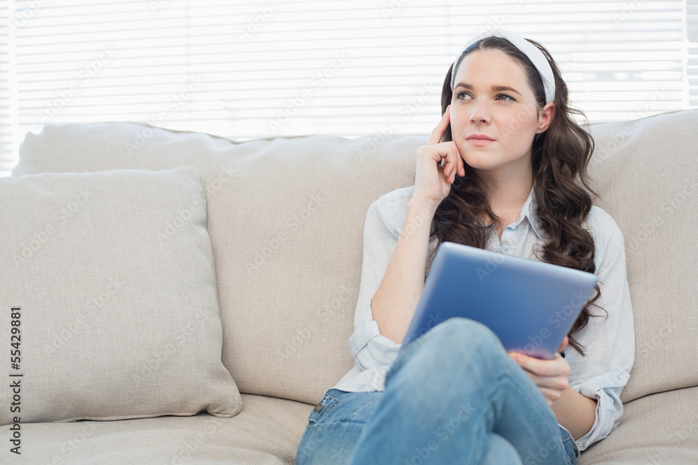 Thoughtful casual woman on cosy couch using tablet pc Thoughtful casual woman on cosy couch using tablet pc