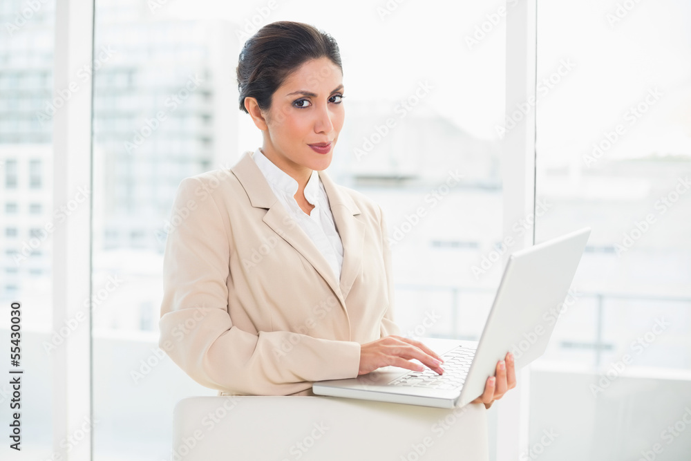 Smiling businesswoman standing behind her chair holding laptop Smiling businesswoman standing behind her chair holding laptop