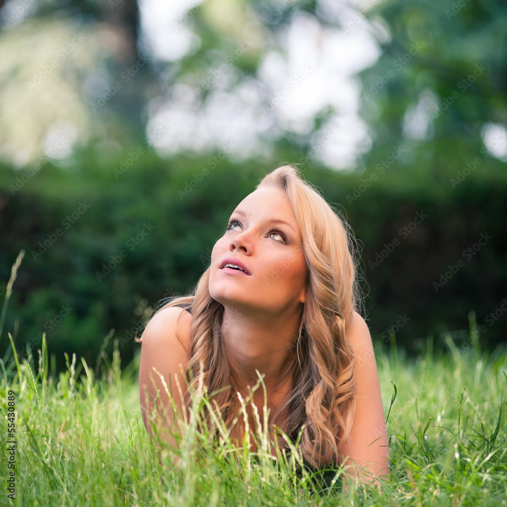 Beautiful blonde girl lying on grass outdoors in a park. Beautiful blonde girl lying on grass outdoors in a park.
