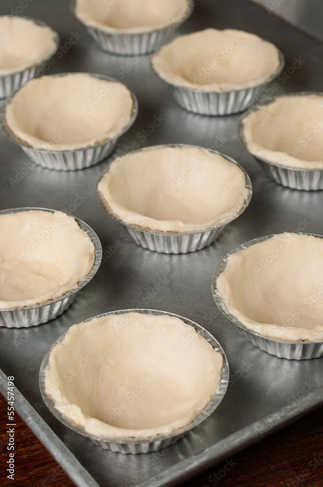 Raw dough in tartlet tins on baking tray.