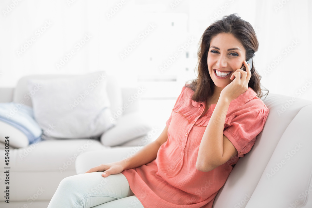 Smiling brunette sitting on her sofa on the phone Smiling brunette sitting on her sofa on the phone