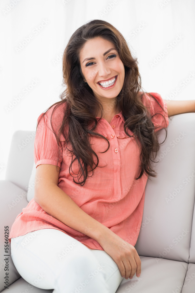Beautiful brunette sitting on her couch smiling at camera Beautiful brunette sitting on her couch smiling at camera