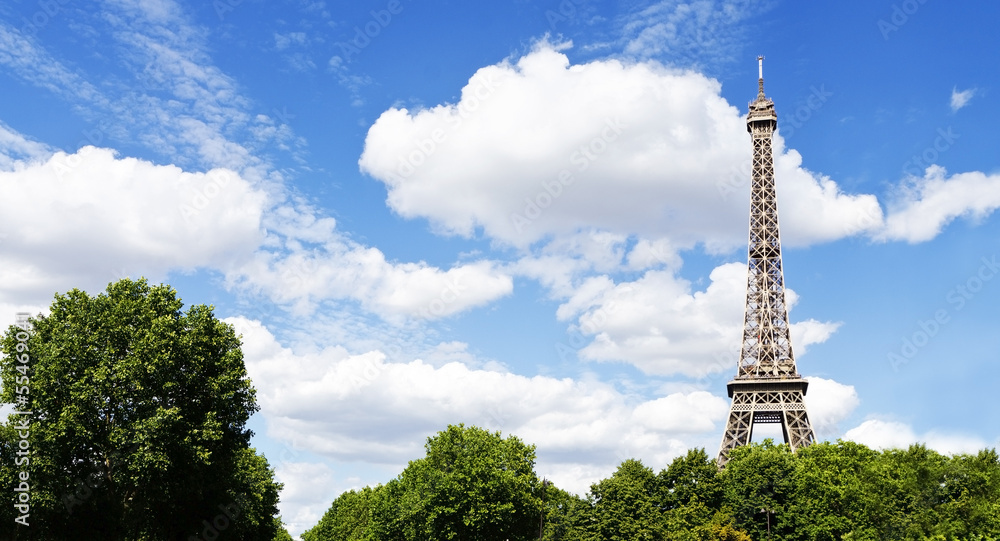 Eiffel tower above trees and blue sky