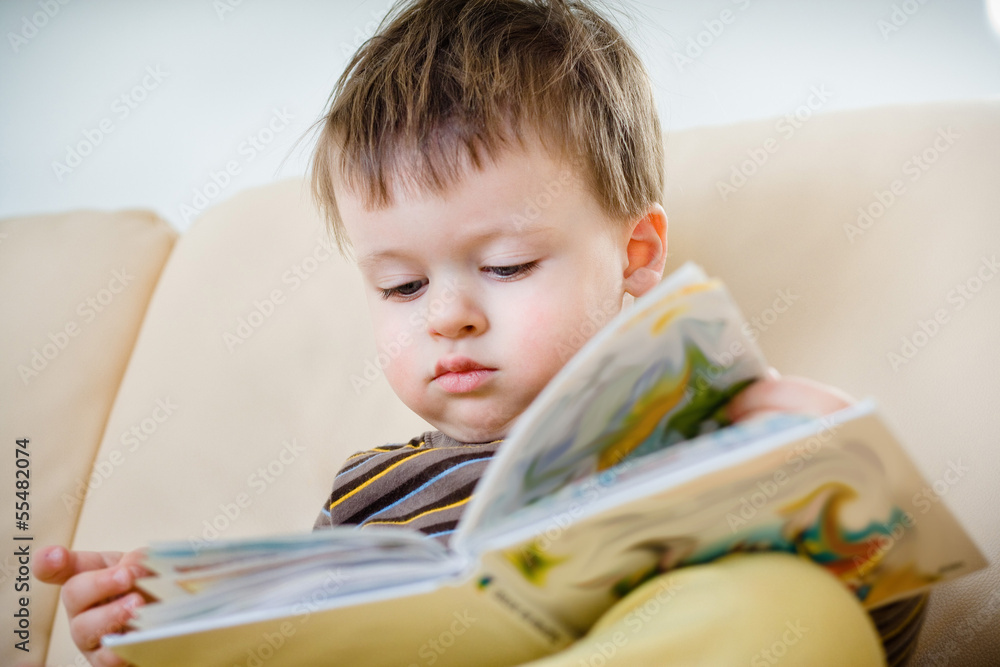 Cute little boy reading book on sofa Cute little boy reading book on sofa