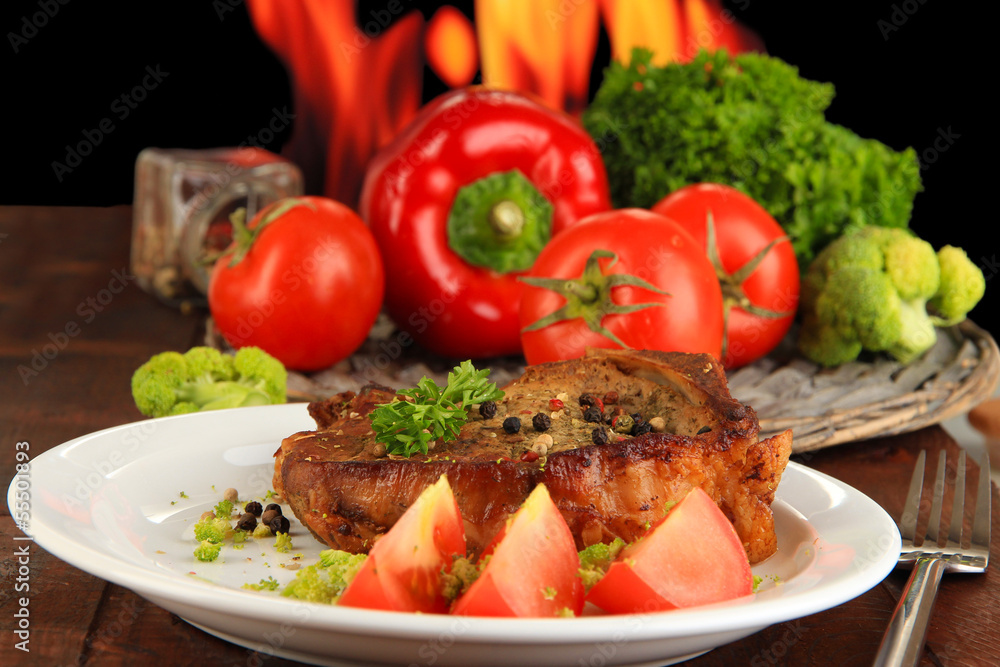 Piece of fried meat on plate on wooden table on fire background Piece of fried meat on plate on wooden table on fire background