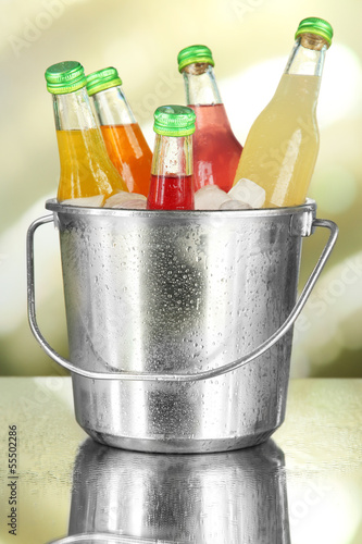 Bottles with tasty drinks in bucket with ice cubes, in bright