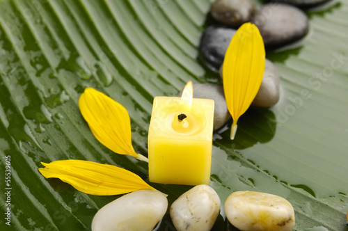 Candle and stones with flower petalson banana leaf