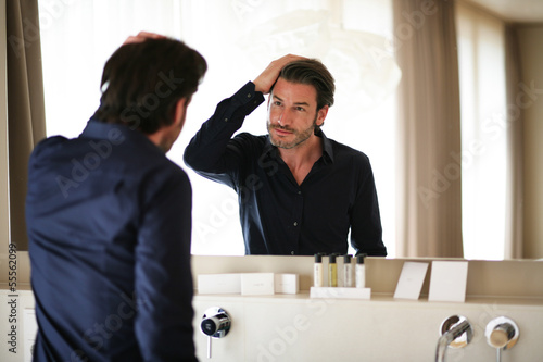 Mann begutachtet sich im Spiegel photo