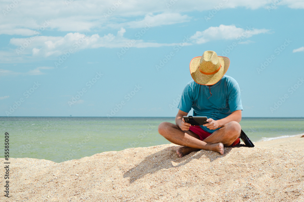 Young man sitting at seaside with tablet computer and resting