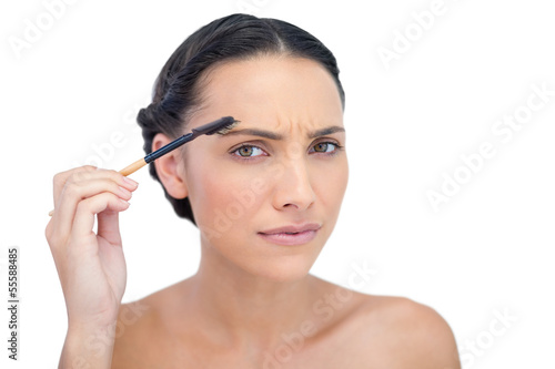 Frowning young brunette using eyebrow brush