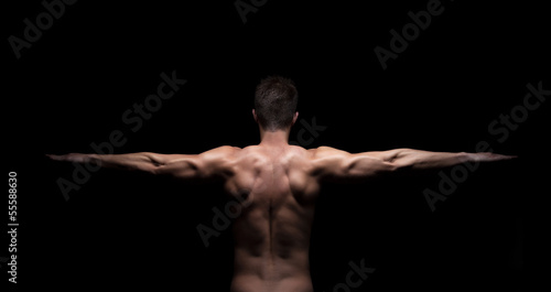 Muscular man with arms streched out on black background