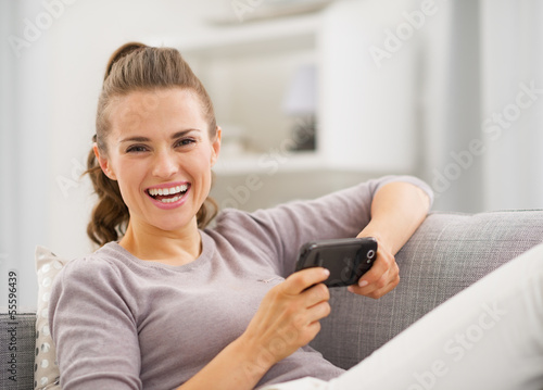 Smiling young woman reading sms while sitting on sofa