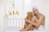 Big baby. Infant adult man in diaper holding teddy bear while si