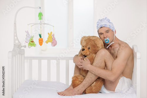 Big baby. Infant adult man in diaper holding teddy bear while si