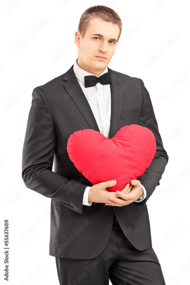 Young handsome man wearing black suit and holding a red heart Young handsome man wearing black suit and holding a red heart