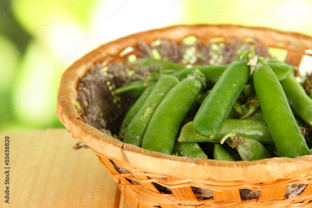 Green peas in basket on wooden table on nature background Green peas in basket on wooden table on nature background