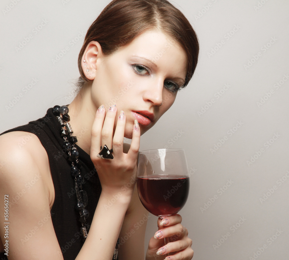 Young woman with a wineglass near the wall, isolated on grey Young woman with a wineglass near the wall, isolated on grey