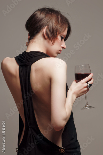 Young woman with a wineglass near the wall, isolated on grey