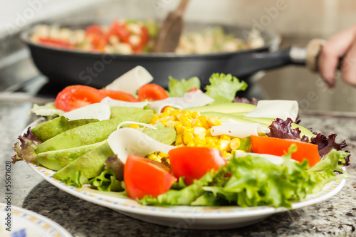 Closeup of fresh salad dish and female cooking in a pan