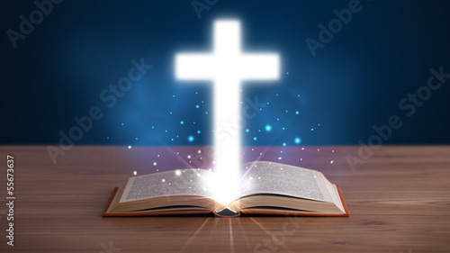 Open holy bible with glowing cross in the middle