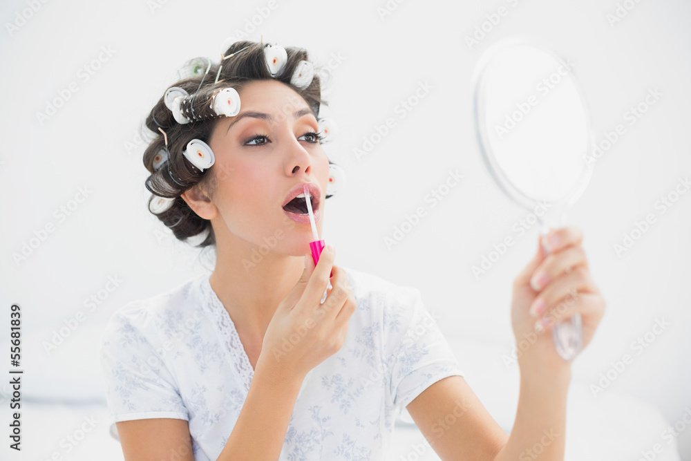 Pretty brunette in hair rollers holding hand mirror and applying Pretty brunette in hair rollers holding hand mirror and applying