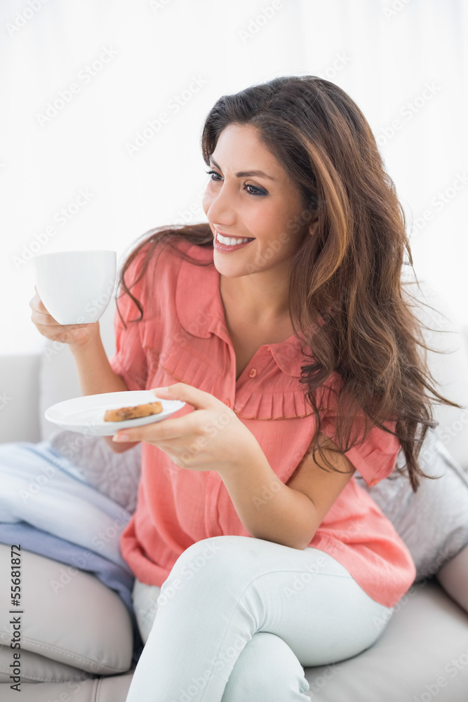 Pretty brunette sitting on her sofa holding cup and saucer Pretty brunette sitting on her sofa holding cup and saucer