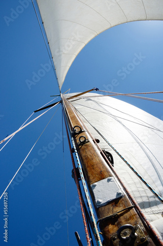 Old wooden mast and white sail, view from deck of boat