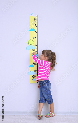 Little girl measuring height against wall in room photo