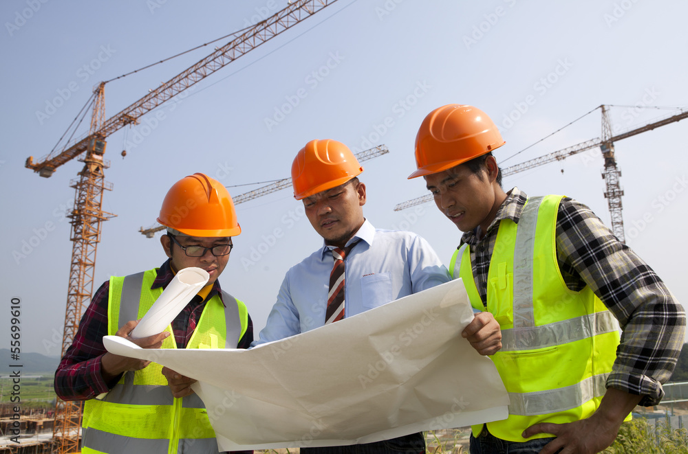 Architects at a construction site looking at blueprint Architects at a construction site looking at blueprint