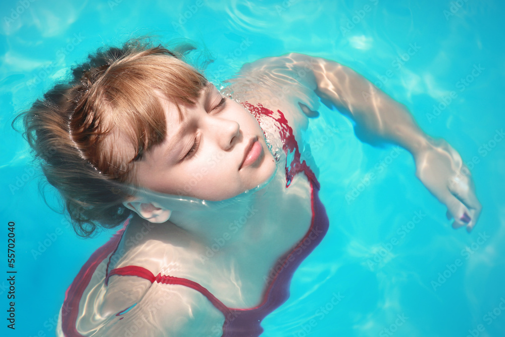 Little blond girl swims relaxed with closed eyes