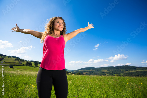 Young woman holding arms up against blue sky