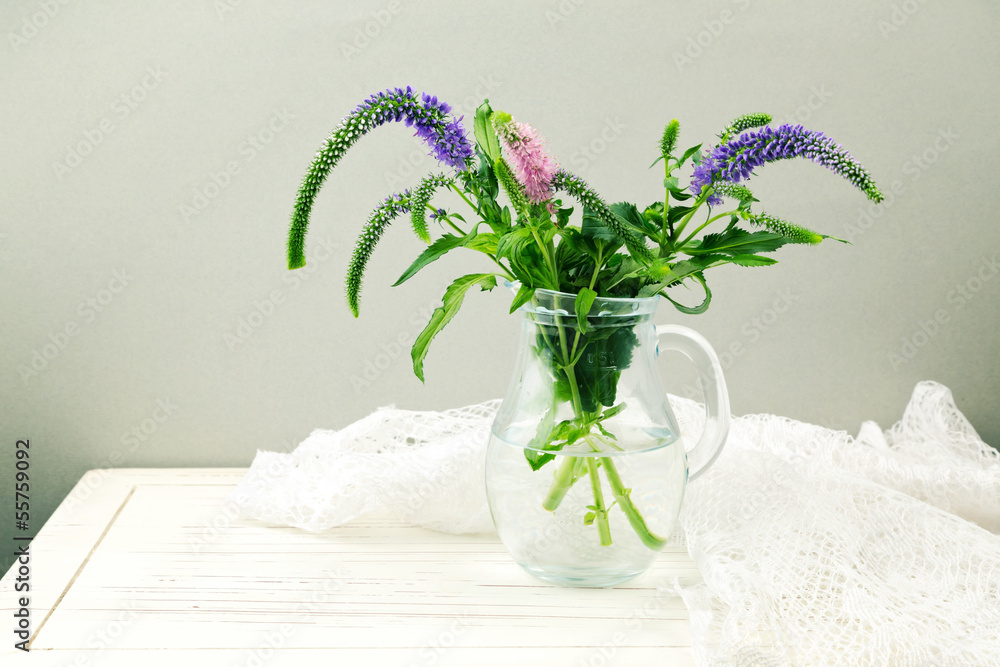 Fototapeta Flowers in glass jug on wooden table with lace textile