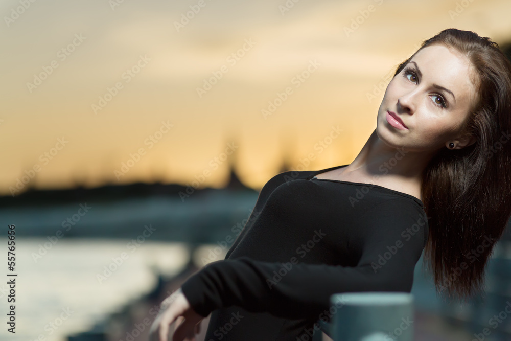 A young woman in a black dress leaning on the railing